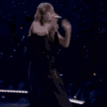 a woman in a black dress is singing into a microphone while dancing on a stage .