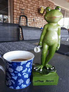 a figurine of a frog holding a cup next to a cup of coffee