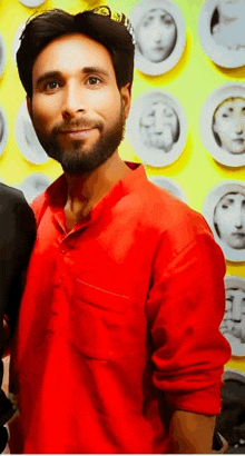 a man in a red shirt is standing in front of a wall with plates with faces on them .