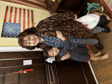 a woman in a leopard print jacket holds a little girl in front of an american flag