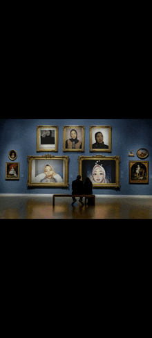 a couple sits on a bench in front of a wall of framed portraits