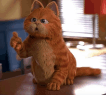 garfield the cat is sitting on a table and pointing at the camera