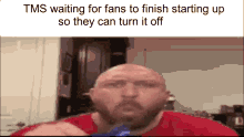 a bald man with a beard is sitting in front of a refrigerator in a kitchen eating chips .