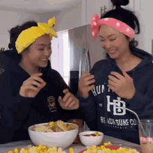 two women are sitting at a table with bowls of food and one is wearing a shirt that says beach surf co.