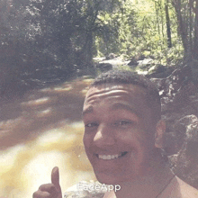 a man is smiling and giving a thumbs up in front of a river and trees