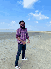 a man in a plaid shirt and white sandals stands on the beach