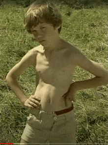 a young boy standing in a field with his hands on his hips