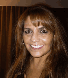 a woman with brown hair and hoop earrings smiles for the camera