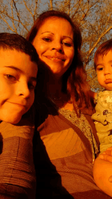 a woman holds two children in her arms and smiles at the camera