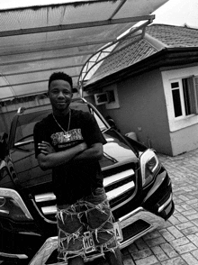 a black and white photo of a young man standing in front of a car with a license plate that says tmg