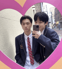 two men in suits and ties are taking a picture of themselves in a heart shaped mirror