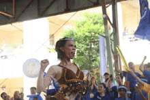 a cheerleader with a crown on her head is cheering in front of a crowd that is wearing blue