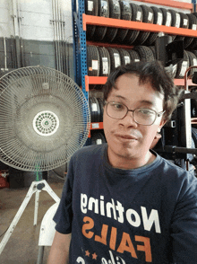 a man wearing glasses and a shirt that says " painton " is standing in front of a fan