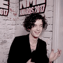 a man with curly hair is standing in front of a brick wall with a sign that says awards 2017 on it .