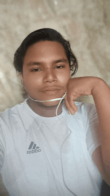 a man wearing a white adidas shirt takes a selfie with his hand on his chin