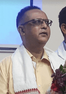 a man wearing glasses and a white scarf holds a bouquet of flowers