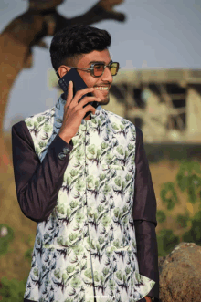 a young man wearing sunglasses and a floral vest talks on a cell phone