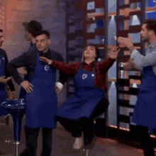 a woman is sitting on a bar stool with her arms outstretched in front of a group of people wearing aprons .