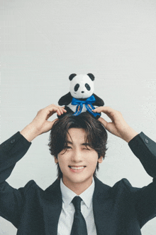 a man in a suit and tie holds a stuffed panda bear on top of his head