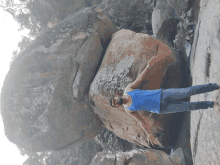 a man in a blue tank top is standing next to a large rock