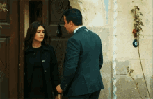 a man in a suit holds a woman 's hand in front of a door