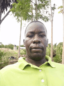 a man wearing a green shirt is standing in front of trees