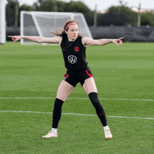 a female soccer player stands on a field with her arms outstretched and a vw logo on her shirt