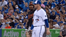 two baseball players are standing next to each other in a stadium . one is wearing a blue jays jersey .