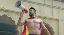 a shirtless man is holding a megaphone and wearing a cape .