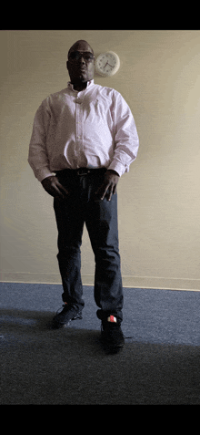 a man in a white shirt and black jeans stands in front of a clock that shows the time as 4:20