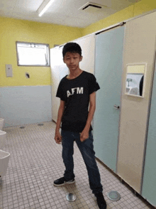 a young boy is standing in a public restroom wearing a black shirt and jeans .