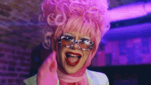 a drag queen wearing a pink wig , sunglasses and a pink scarf .