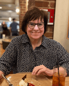 a woman in glasses sits at a table with a plate of food