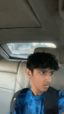 a young man in a blue shirt is sitting in the back seat of a car