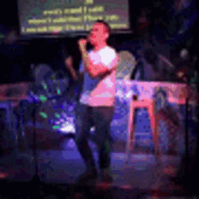 a man is singing into a microphone on a stage in front of a screen .