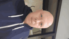 a bald man wearing a blue hoodie looks at the camera