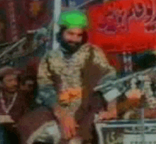 a man with a green turban is standing in front of a red sign that says ' a ' on it