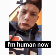 a man wearing a hat and a hoodie with the words " i 'm human now " on the bottom