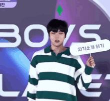 a young man in a green and white striped sweater is holding a sign in front of a sign that says boys .