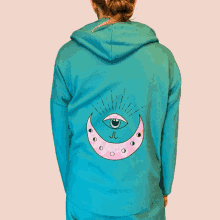 a woman wearing a green hoodie with a pink crescent moon with an eye on it