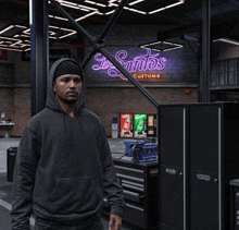 a man in a black hoodie stands in front of a neon sign that says santos customs