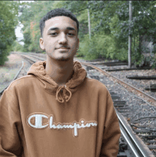 a man wearing a brown champion sweatshirt stands on train tracks