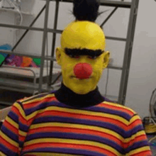 a person wearing a striped shirt and a yellow face painted like sesame street bert