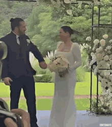 a bride and groom are holding hands during their wedding ceremony and the bride is holding a bouquet of white flowers