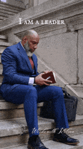 a man in a suit sits on a set of stairs reading a book with the words " i am a leader " above him