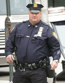 a fat police officer is standing in front of a bus holding a gun .