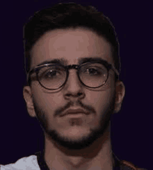 a young man with a beard and glasses is looking at the camera with a serious look on his face .