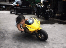 a little girl is riding a yellow motorcycle with the word ducati on the side