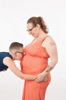 a man kisses a pregnant woman 's belly with a tattoo on her arm that says i twin