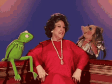 a woman in a red dress sits next to a green kermit the frog and a pig puppet